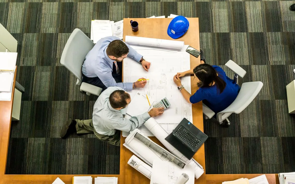 Three colleagues reviewing construction plans around an office table.