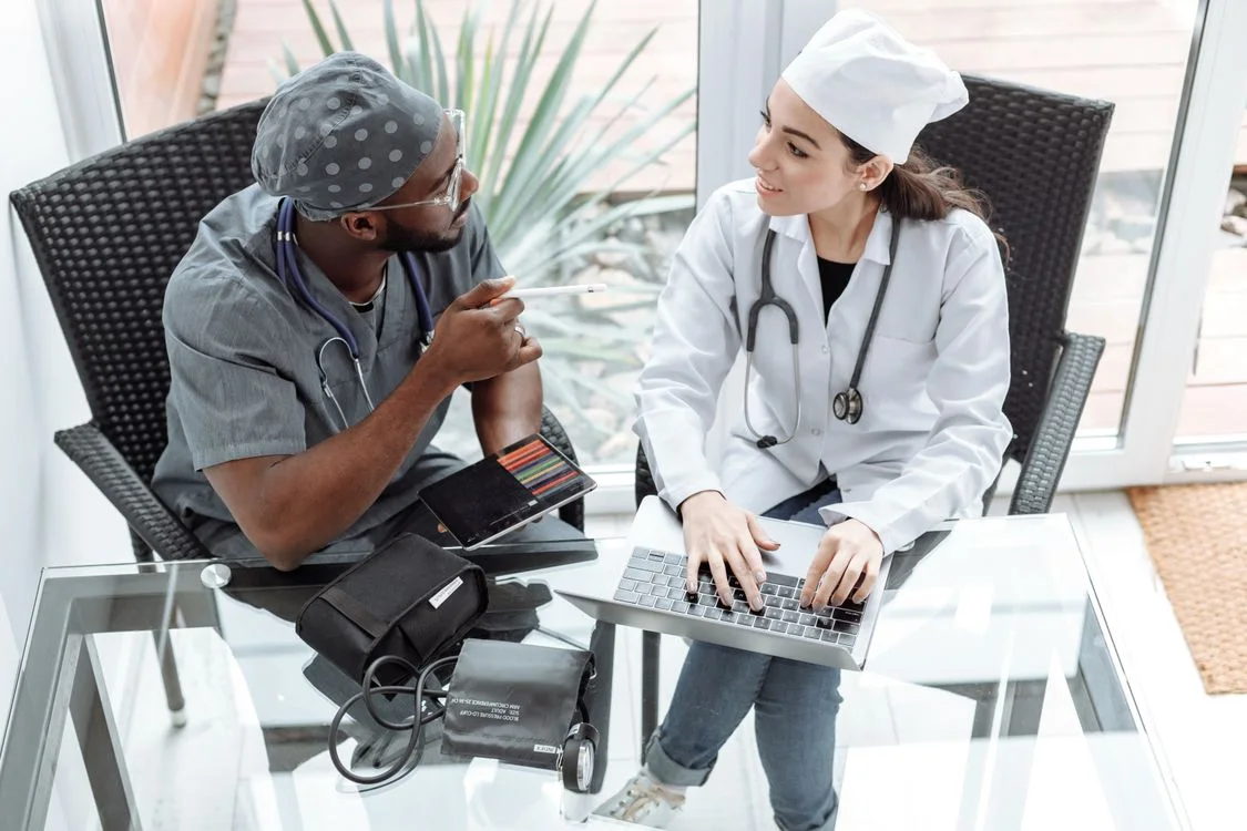 Two healthcare professionals discussing work with a laptop and tablet.