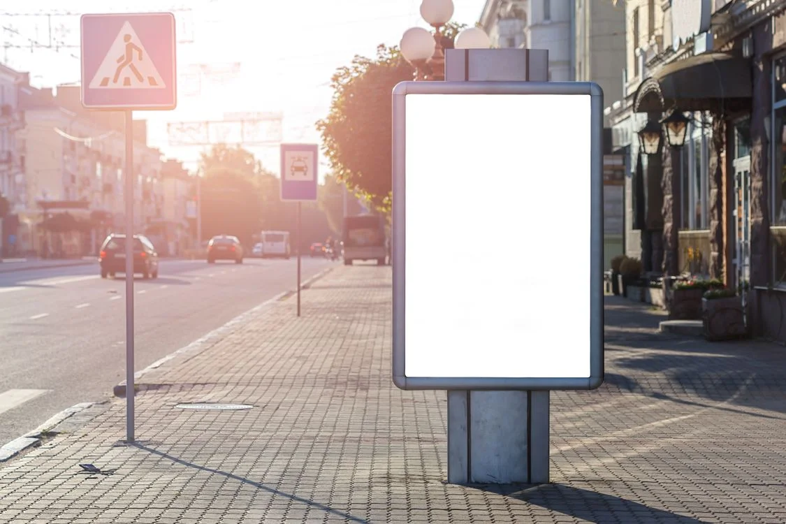 An outdoor advertising display on a sunlit city pavement.