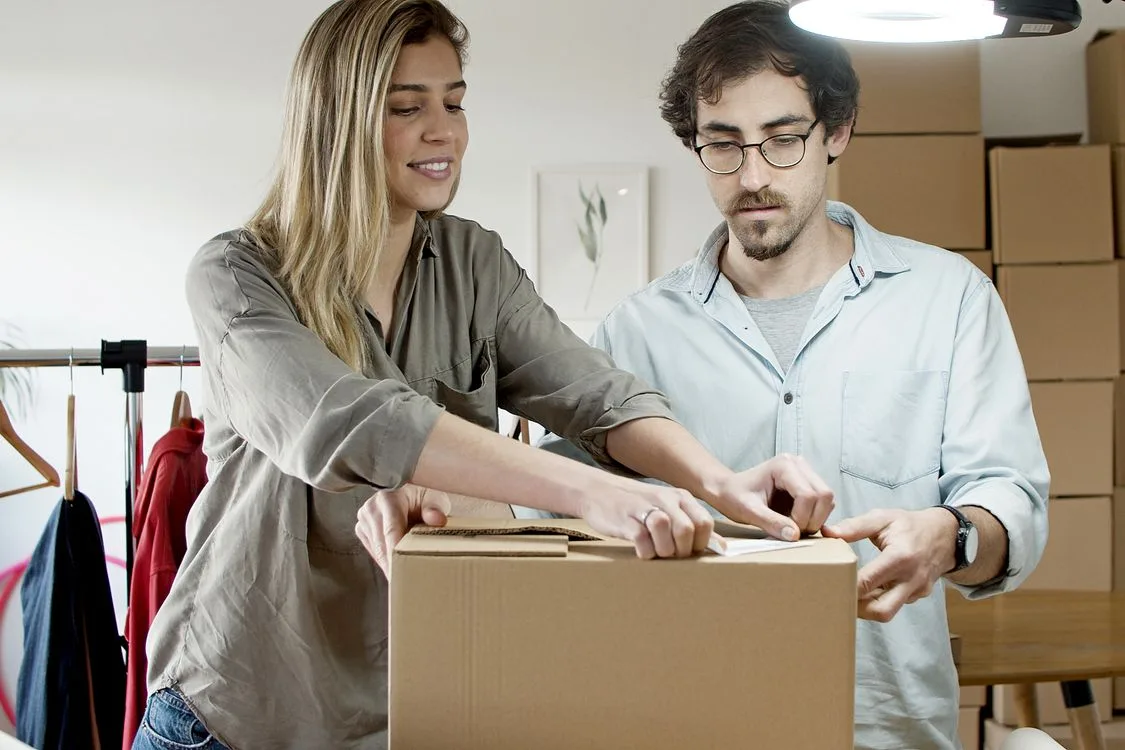 Two colleagues packing and labelling a customer order beside clothing stock.