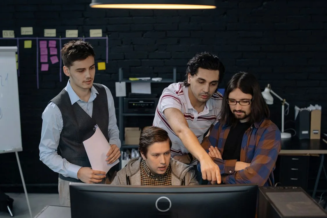 Four colleagues discussing a technical project together at a desktop computer.